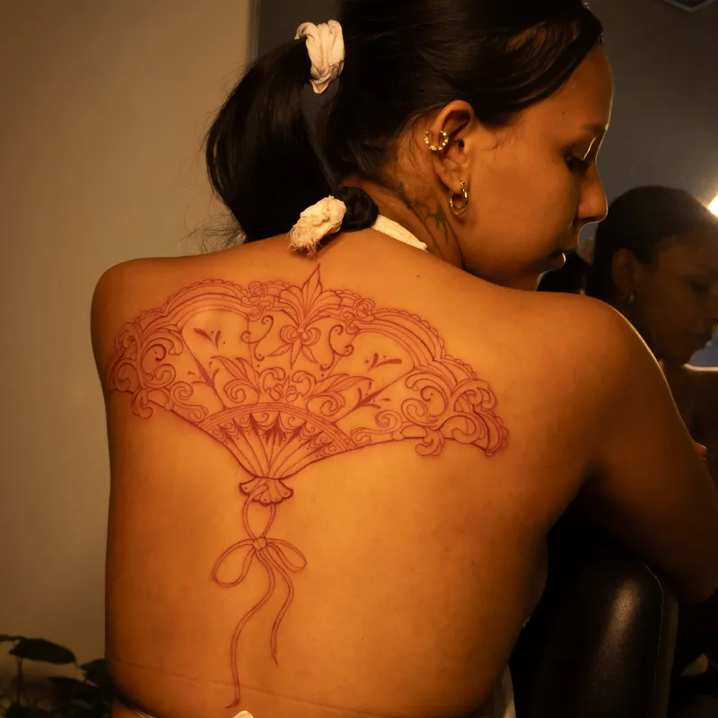 Ornate fine-line floral fan tattoo on client back and spine